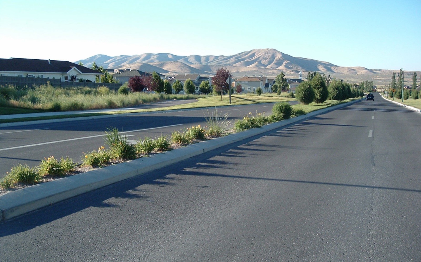 Pony Express Parkway, a landscaped divided road, running past two-story homes toward dry rounded mountains in Eagle Mountain, Utah