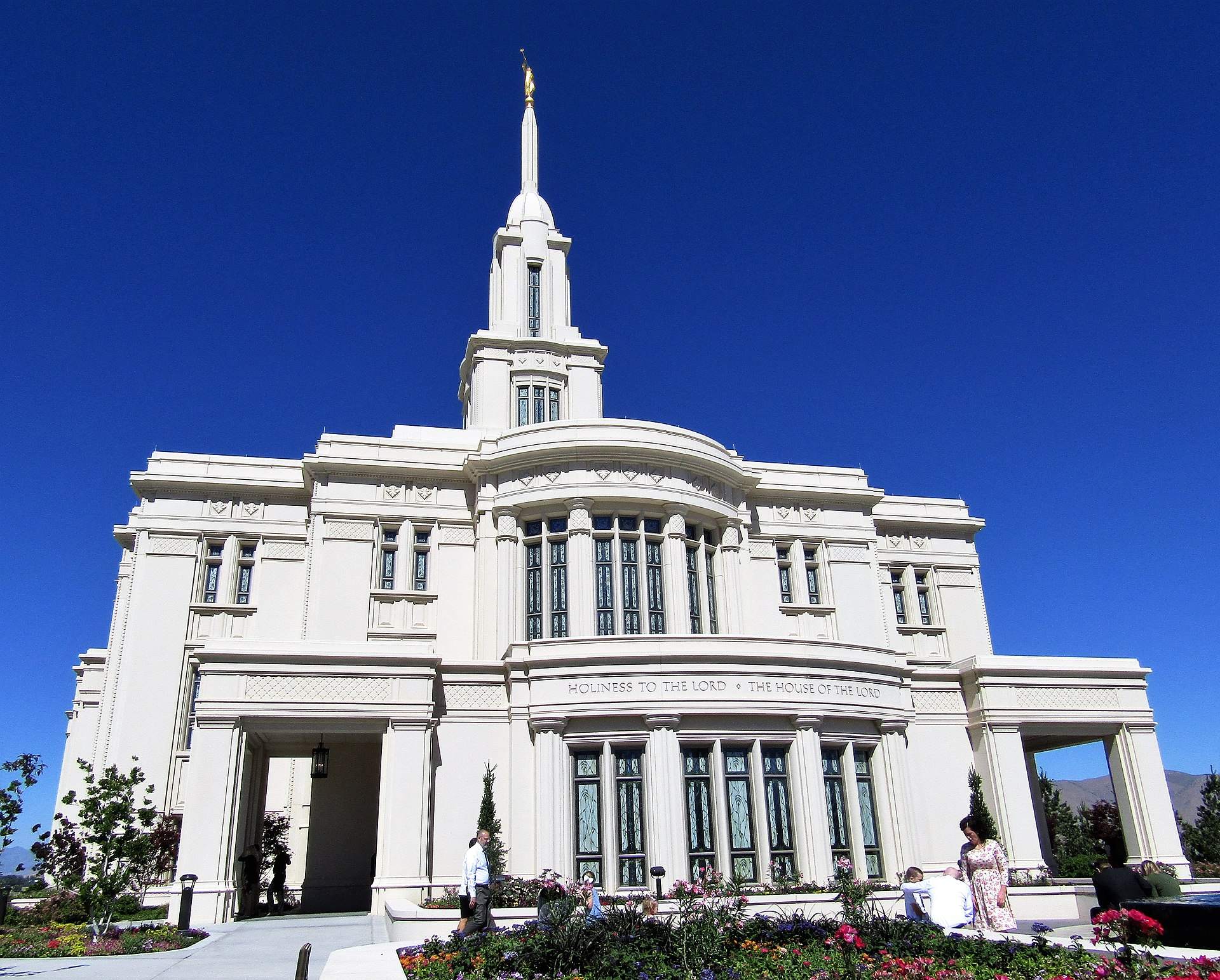 The east side of the Payson Utah Temple, a white temple with a single spire, under a blue sky